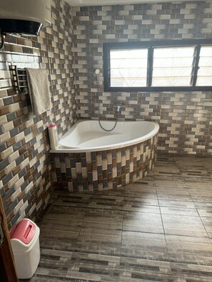 A bathroom with a freestanding bathtub, a window, and a tiled floor. - Larosa Executive Guest House (Kumasi)