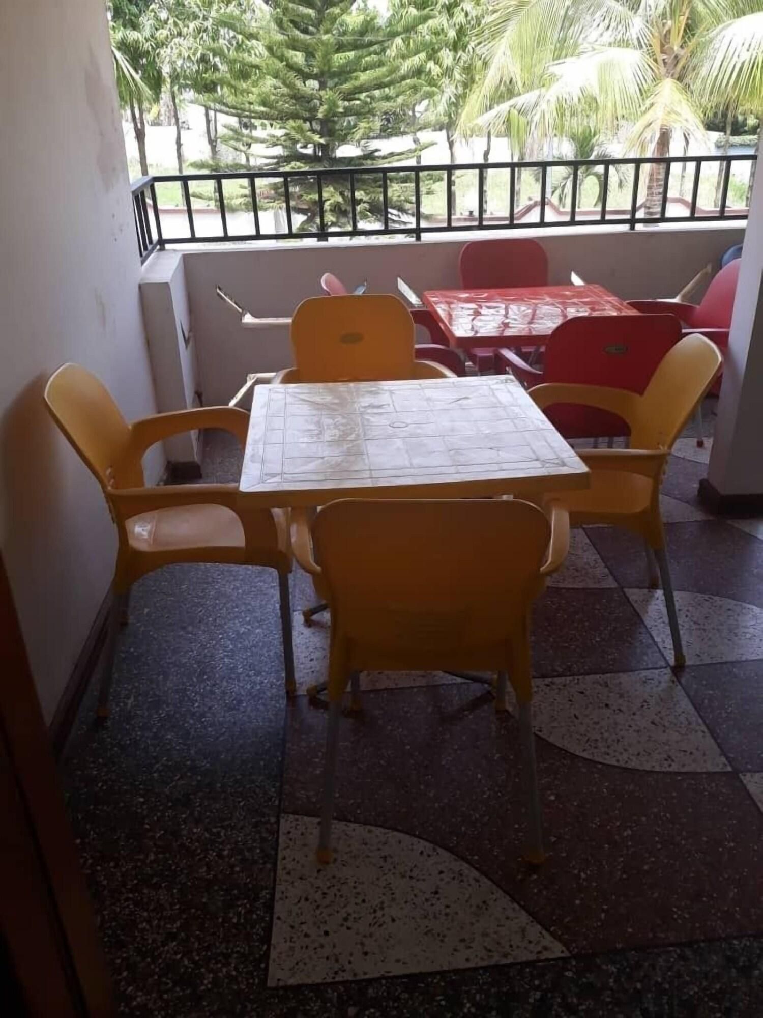 Una pequeña zona de estar al aire libre con una mesa y sillas, piso de baldosas y vistas a palmeras.