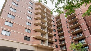 Un immeuble en briques de plusieurs étages, doté de balcons, d’un espace de stationnement couvert et agrémenté de quelques espaces verts.
