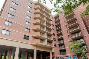 A multi-story brick building with balconies, a covered parking area, and some greenery. - Blueground | Clarendon, gym, nr Arlington Cemetery (Arlington)
