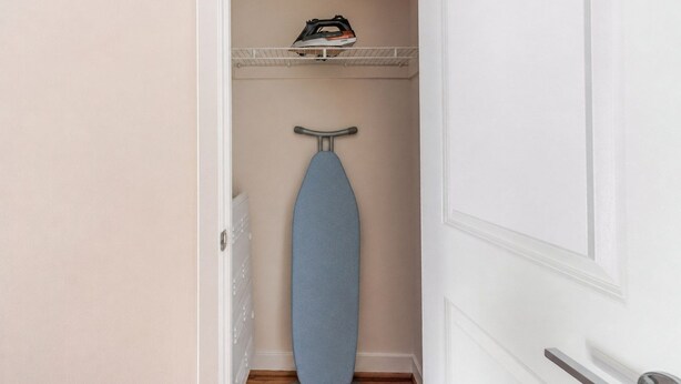 Un couloir étroit avec une planche à repasser bleue et un fer à repasser posé sur une étagère.
