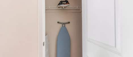 A narrow hallway with a blue ironing board and an iron on a shelf.