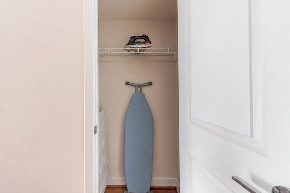 A narrow hallway with a blue ironing board and an iron on a shelf. - Blueground | Clarendon, gym, nr Arlington Cemetery (Arlington)