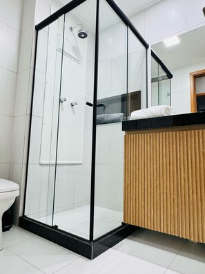 A modern bathroom with a glass-enclosed shower, a wooden vanity, and a white toilet. - 2-bedroom apartment in the Malia Beach Resort in Muro Alto, Porto de Galinhas (Ipojuca)