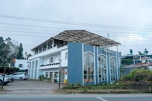 A building with a covered entrance and large windows, surrounded by parked cars and greenery. - Tani Jiwo Hostel (Dieng Kulon)