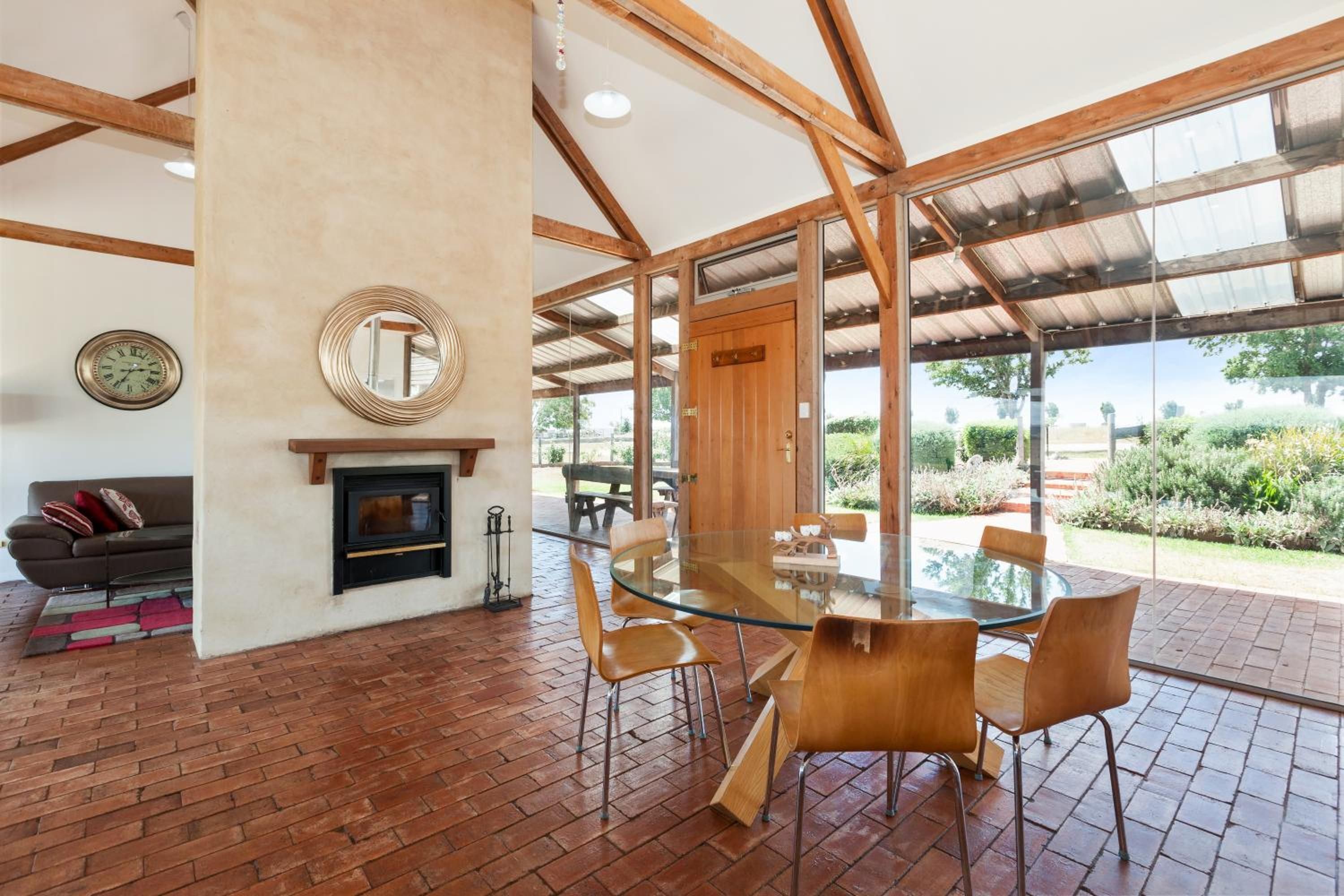 A modern interior with a glass dining table, wooden chairs, a fireplace, and a large window offering a view of the outdoors.