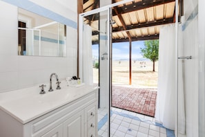 A bathroom with a white vanity, a mirror, and a shower area with a glass door leading to an outdoor patio.