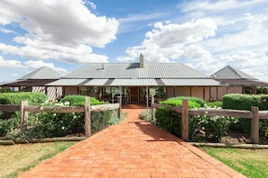 A building with a central entrance, surrounded by a brick pathway, and bordered by wooden fences and greenery.