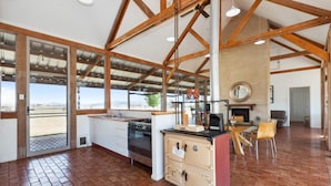 A spacious kitchen with a large island, wooden beams, and a view through the glass doors.