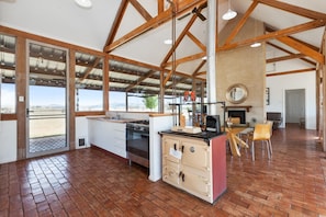 A spacious kitchen with a large island, wooden beams, and a view through the glass doors.