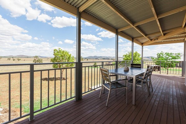 A covered outdoor area with a table and chairs, a view of a field and distant hills.