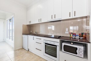 A modern kitchen with white cabinets, a dishwasher, an oven, and a microwave.
