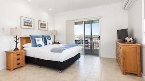 A bedroom with a bed, bedside tables, a TV, and a balcony.