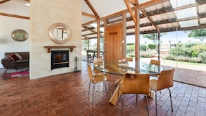 A modern interior with a glass dining table, wooden chairs, a fireplace, and a large window offering a view of the outdoors.