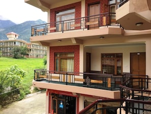 En bygning med flere etager og en balkon, et skilt der angiver en rejse til Himalaya, samt udsigt over et grønt område og fjerne bjerge.