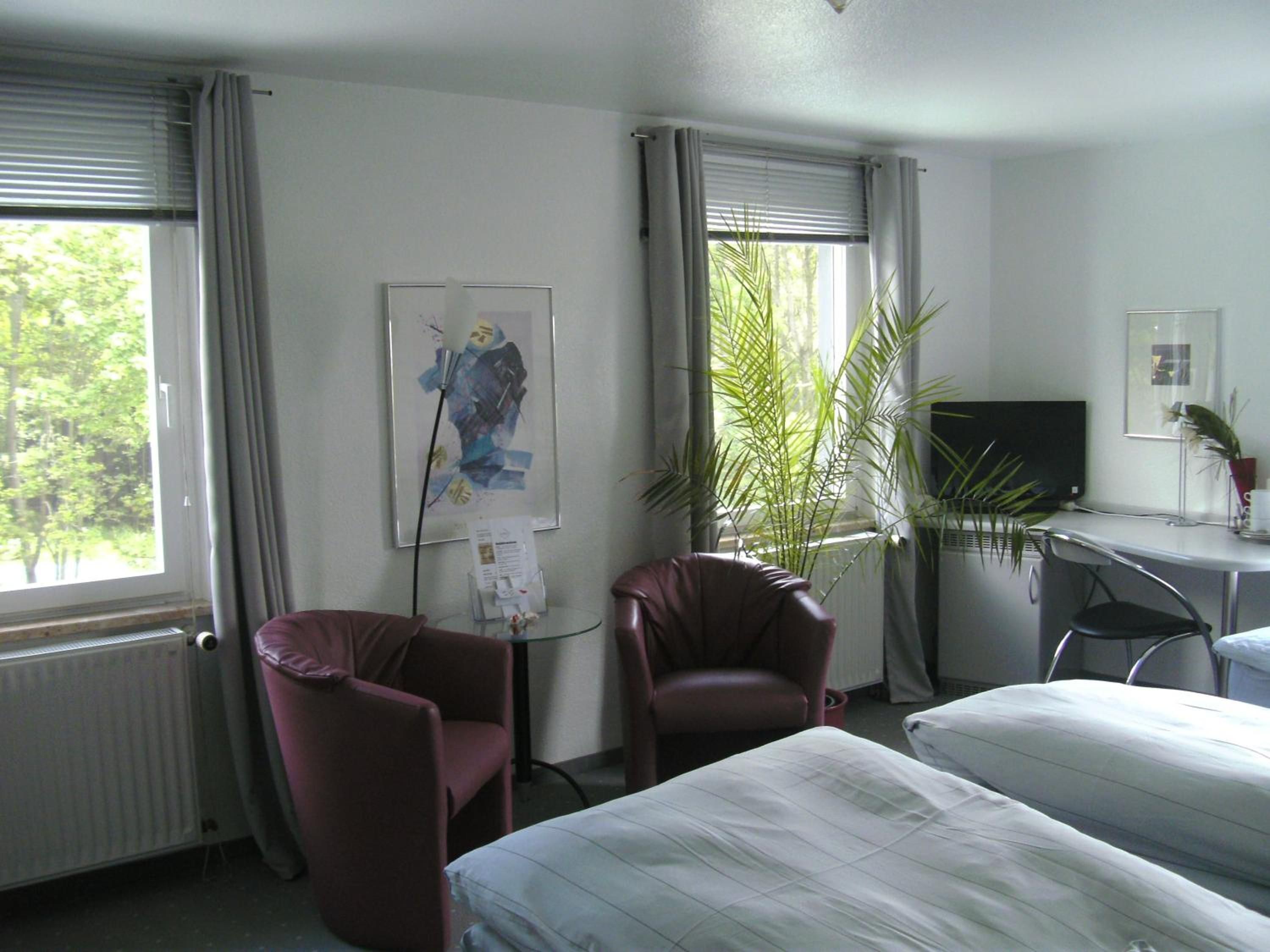 A hotel room with two beds, a desk with a computer, a chair, a radiator, and a window with curtains.