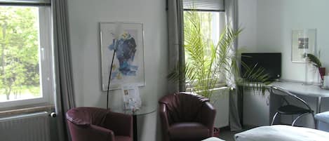 A hotel room with two beds, a desk with a computer, a chair, a radiator, and a window with curtains.