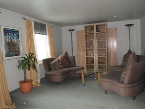 Sala de estar com dois sofás, uma mesa de centro de vidro, uma planta em vaso, um armário com prateleiras e um quadro na parede.