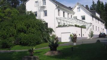 Ein zweistöckiges weißes Gebäude mit sichtbarer Garagentür, einer Treppe und einem kleinen Gartenbereich mit Blumentöpfen.