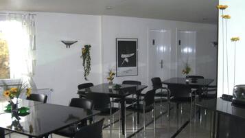 Ein modernes Hotelzimmer mit Essbereich, der Glastische und schwarze Stühle umfasst, einem gerahmten Kunstwerk an der Wand und einem Fenster mit Vorhängen.