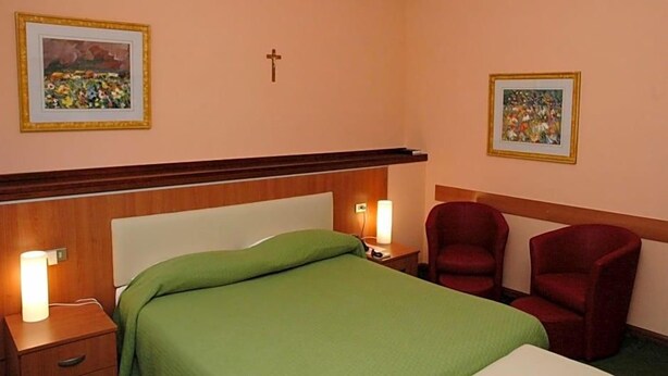 Une chambre d’hôtel avec un lit, deux chaises, une table de chevet avec une lampe et deux tableaux encadrés accrochés aux murs.