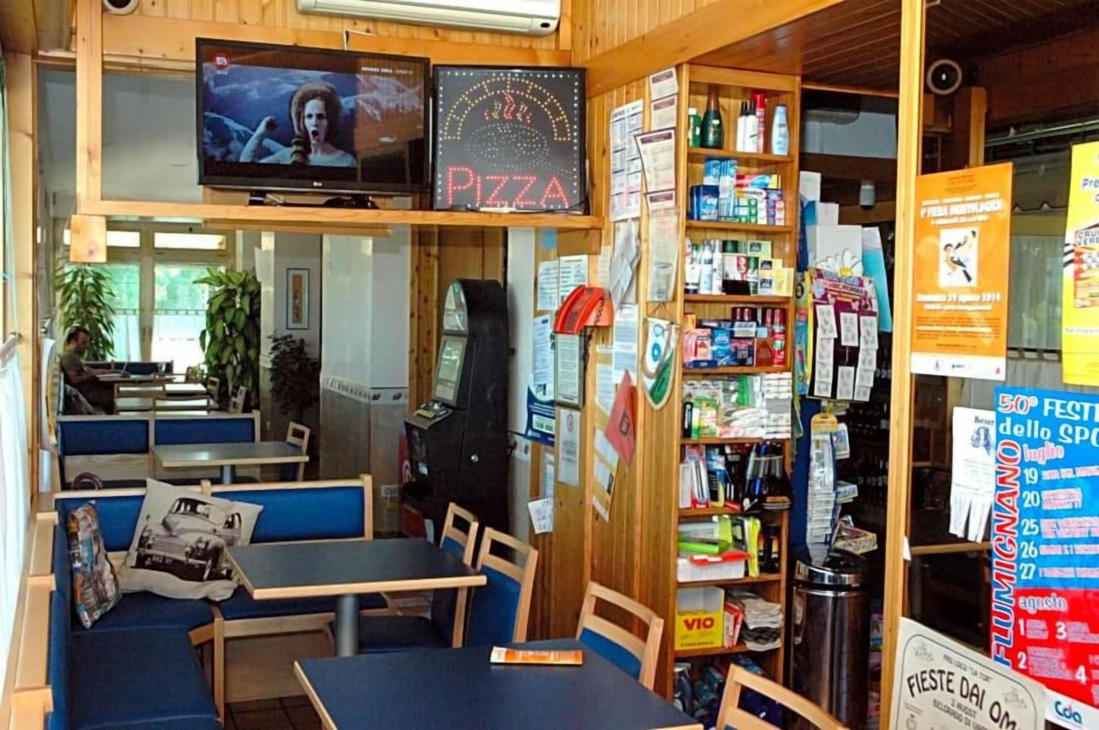 Interior de restaurante con mesas, una pantalla mostrando una película y varios carteles y letreros.