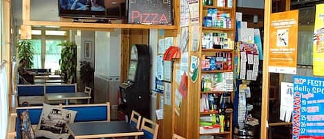 Interior de restaurante con mesas, una pantalla mostrando una película y varios carteles y letreros.