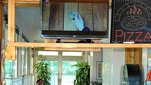 Un restaurant avec des banquettes bleues, un écran de télévision et un panneau lumineux en forme de pizza.