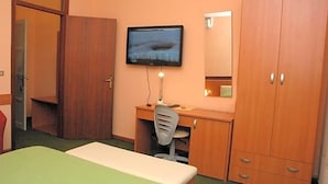 Une chambre d’hôtel comprenant un lit, un bureau avec une chaise, un téléviseur fixé au mur et une armoire.