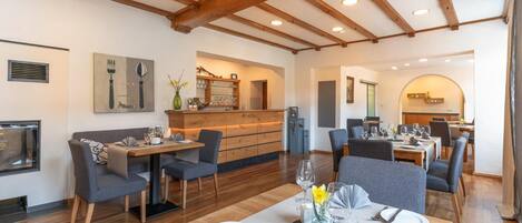 A dining area with wooden beams, a bar, and a kitchen in the background.