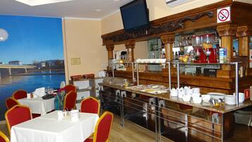 A restaurant with a view of a river, tables with white tablecloths, red chairs, and a bar area with various bottles and glasses.