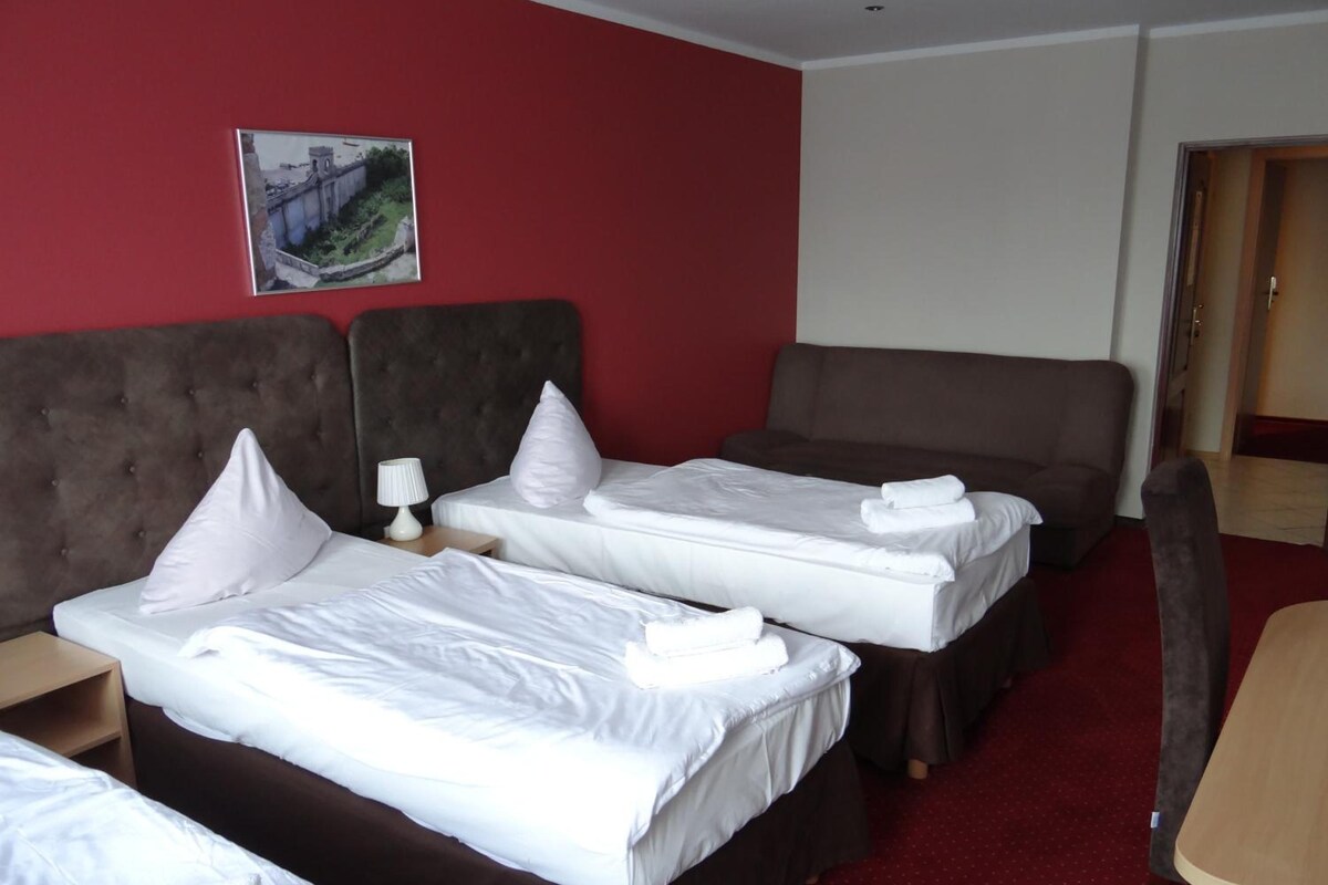 A hotel room with two beds, a sofa, a desk, and a painting on the wall.
