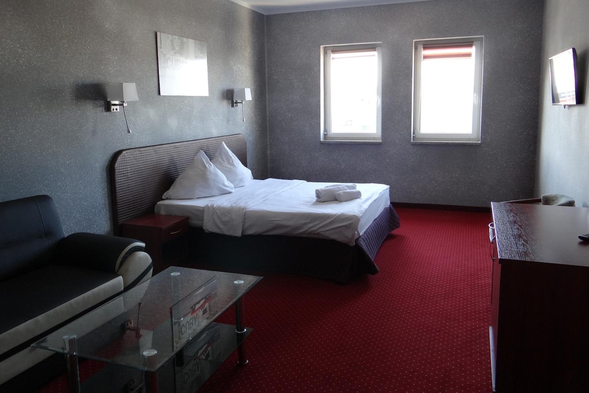 A hotel room with a bed, a desk, a chair, and two windows.