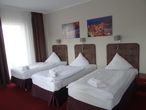 Habitación de hotel con dos camas individuales, un ventanal con cortinas y dos lámparas de pared.