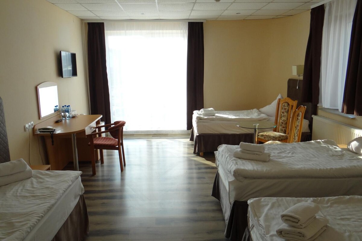 A hotel room with a desk, two beds, a chair, and a large window.
