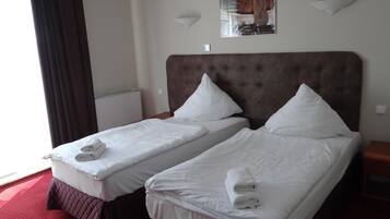 A hotel room with two single beds, each with white linens and towels, a tufted headboard, and a wall-mounted light fixture.