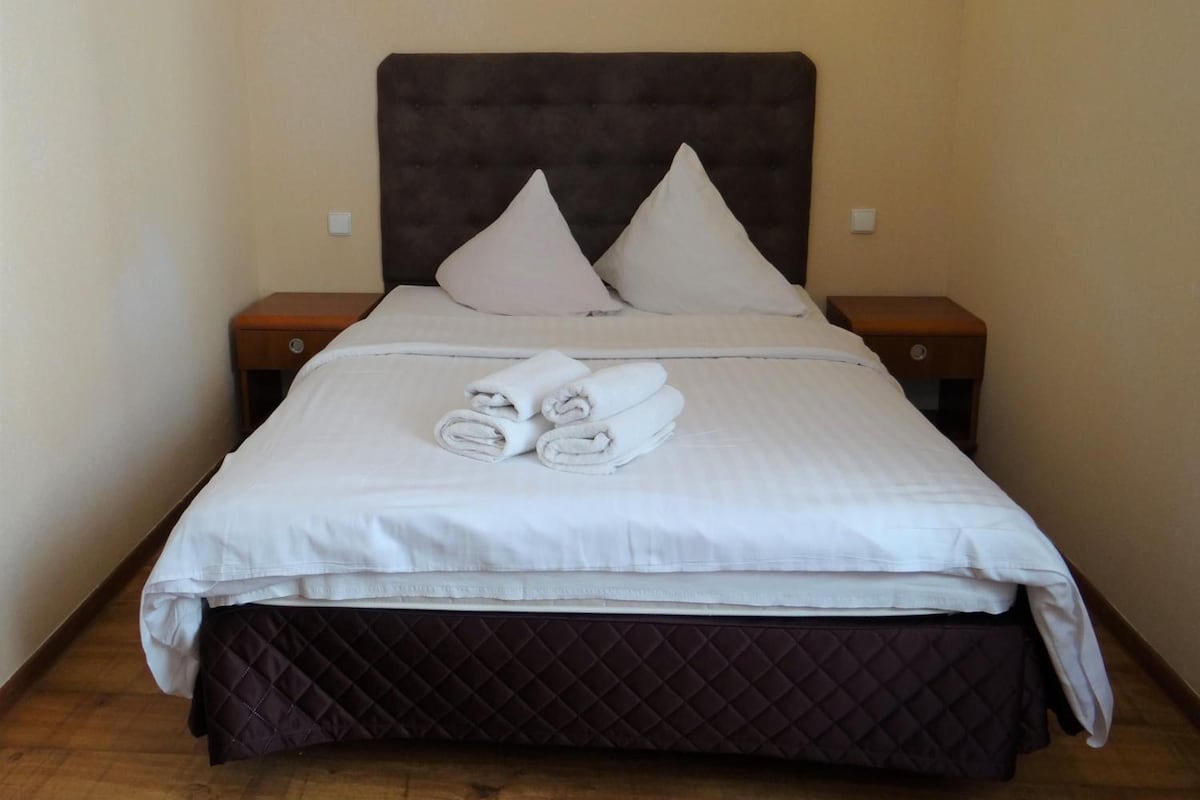 A hotel room with a bed, two bedside tables, and two wall-mounted lights.