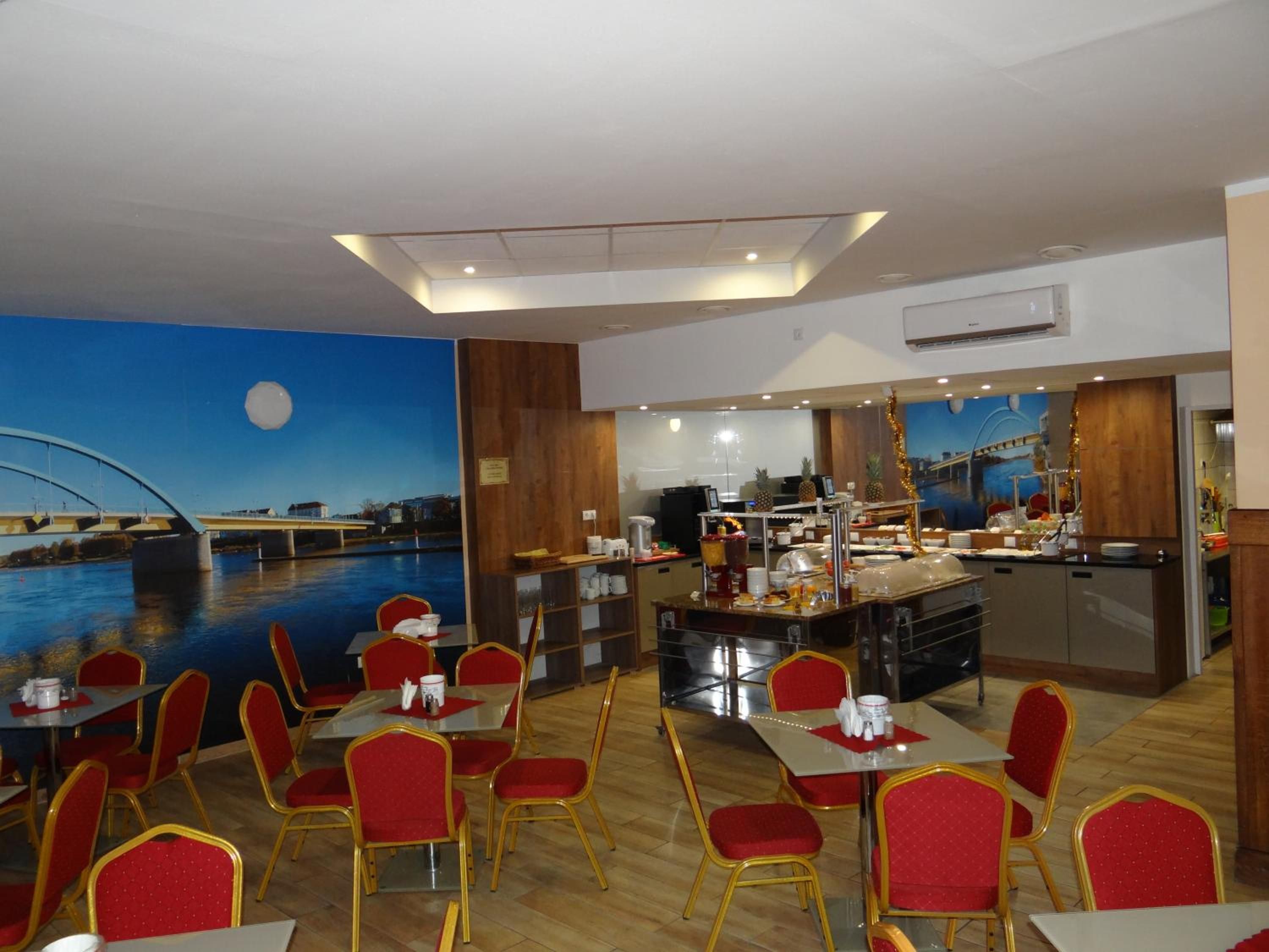 A restaurant with red chairs and tables, a buffet area, and a mural of a bridge and water.