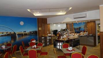 A restaurant with red chairs and tables, a buffet area, and a mural of a bridge and water.