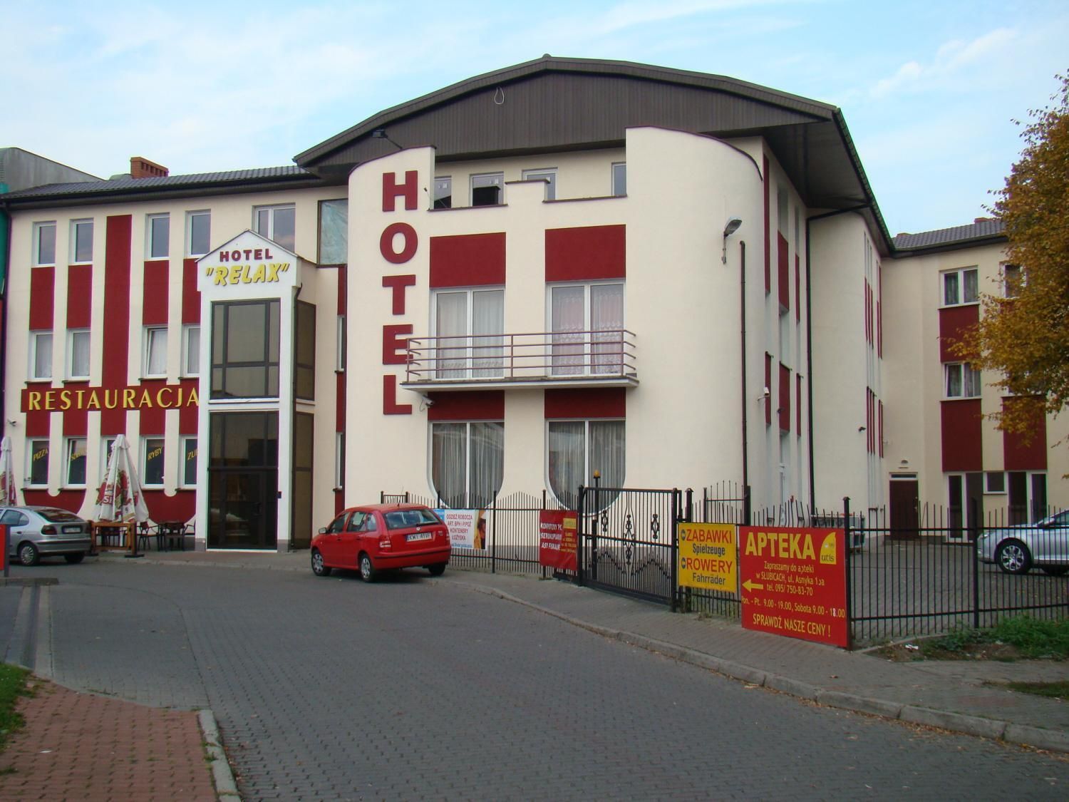 Un hôtel avec une enseigne « HÔTEL » bien visible, une entrée facilement identifiable et une voiture rouge garée devant.