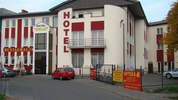 Un hôtel avec une enseigne « HÔTEL » bien visible, une entrée facilement identifiable et une voiture rouge garée devant.