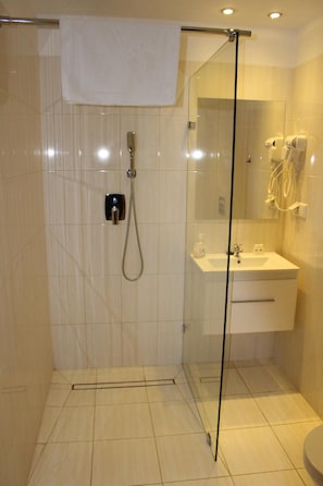 Un baño moderno con cabina de ducha de vidrio, un lavamanos blanco y un espejo.
