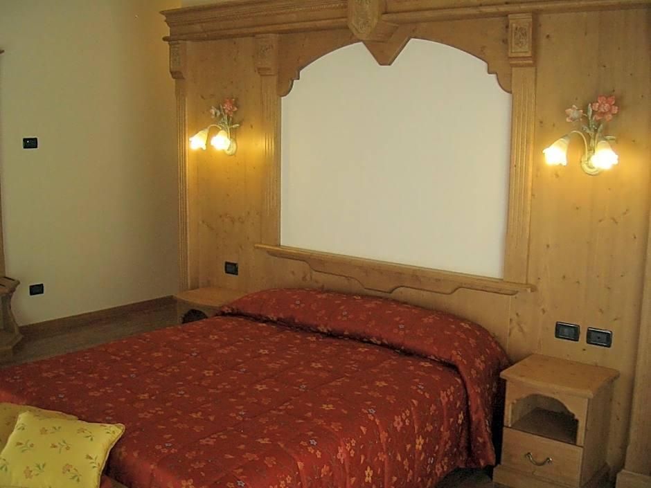 Un dormitorio con cabecera de madera, colcha roja, dos lámparas de pared y una mesita de noche con cajón.