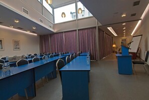 Un salón de conferencias con una larga mesa, sillas, un atril y un amplio ventanal.
