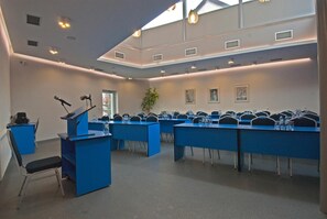 Un salón de conferencias con una mesa larga, sillas, un atril y una planta.