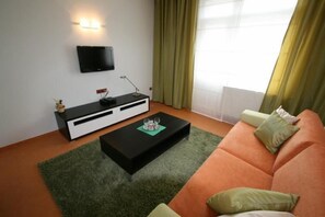 Una sala de estar con un mueble multimedia negro, una mesa de centro negra, un sofá naranja y una alfombra verde.