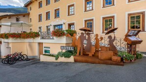 Un edificio de hotel con múltiples ventanas, un balcón con flores y una escultura de figuras.