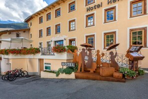 Edifício de hotel com várias janelas, varanda florida e escultura de figuras.