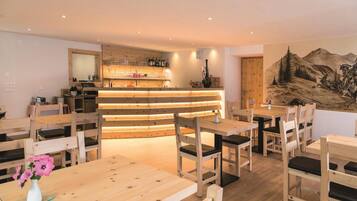 Un ristorante con arredi in legno, un'area bar e un dipinto raffigurante un paesaggio montano alla parete.