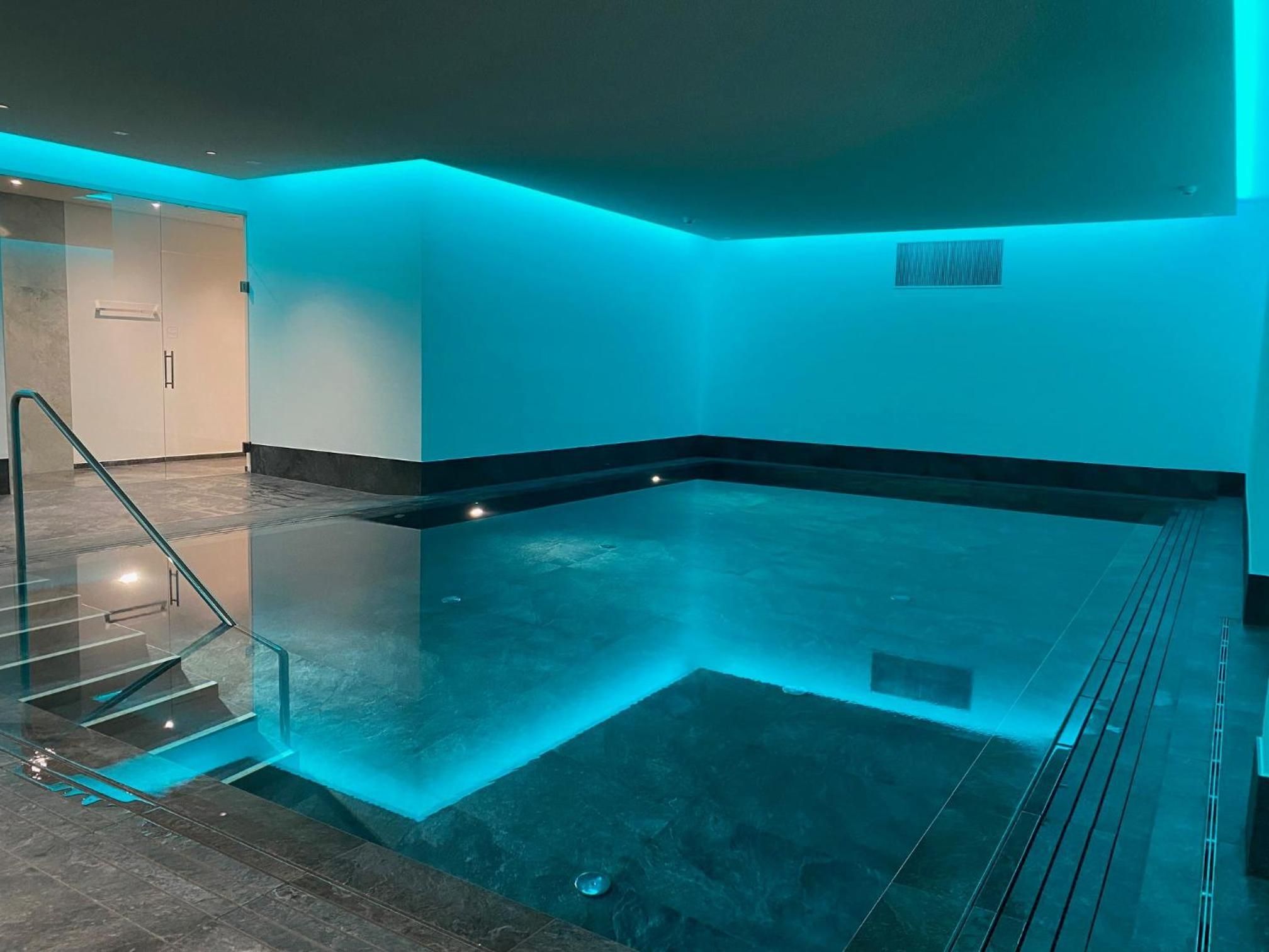 Un espace spa doté d’un jacuzzi aux parois en verre, d’un sol carrelé et d’un escalier menant à un niveau supérieur.